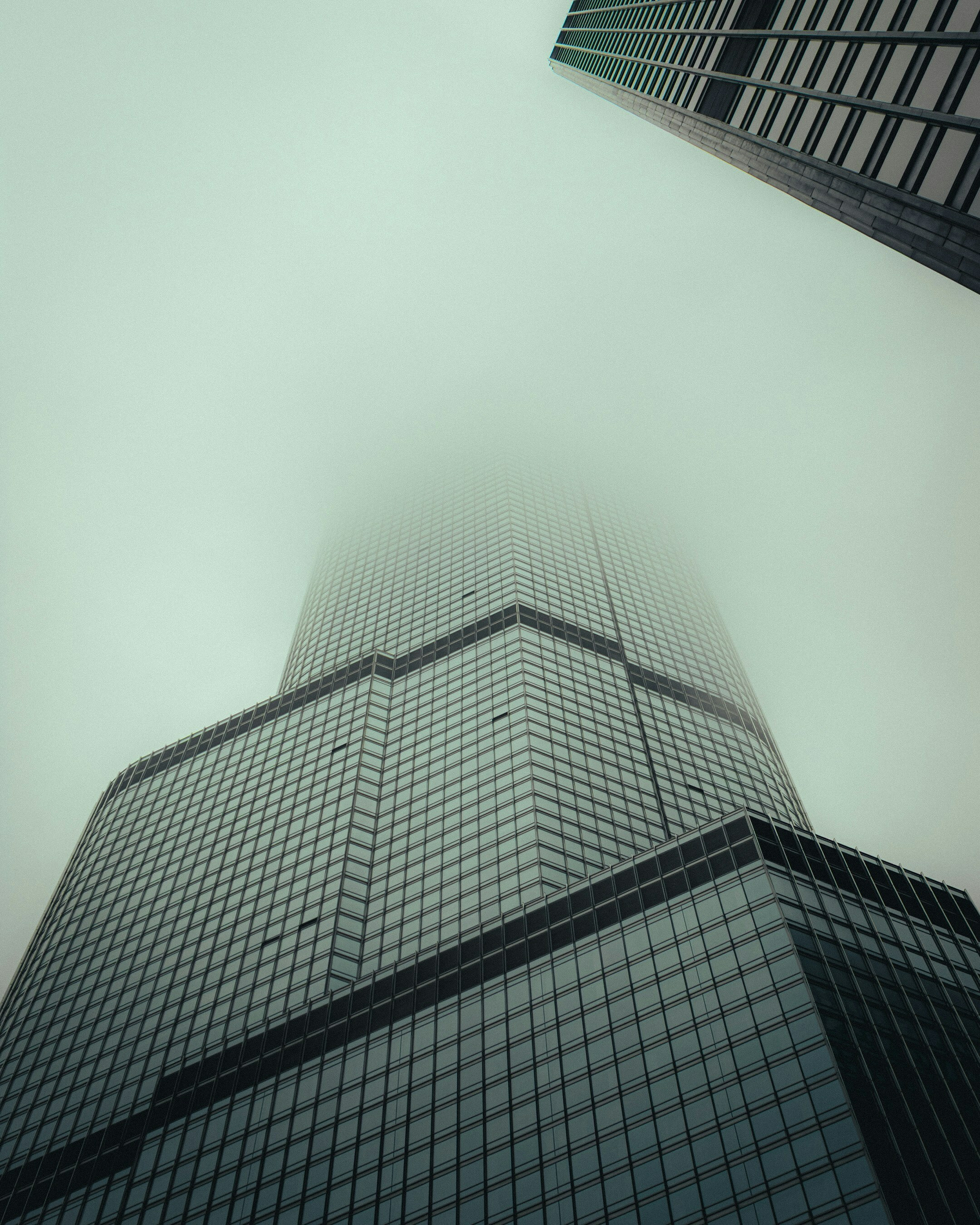 Auto-generated description: A tall, modern skyscraper disappears into a misty sky, with its geometric lines accentuating the cloudy atmosphere.